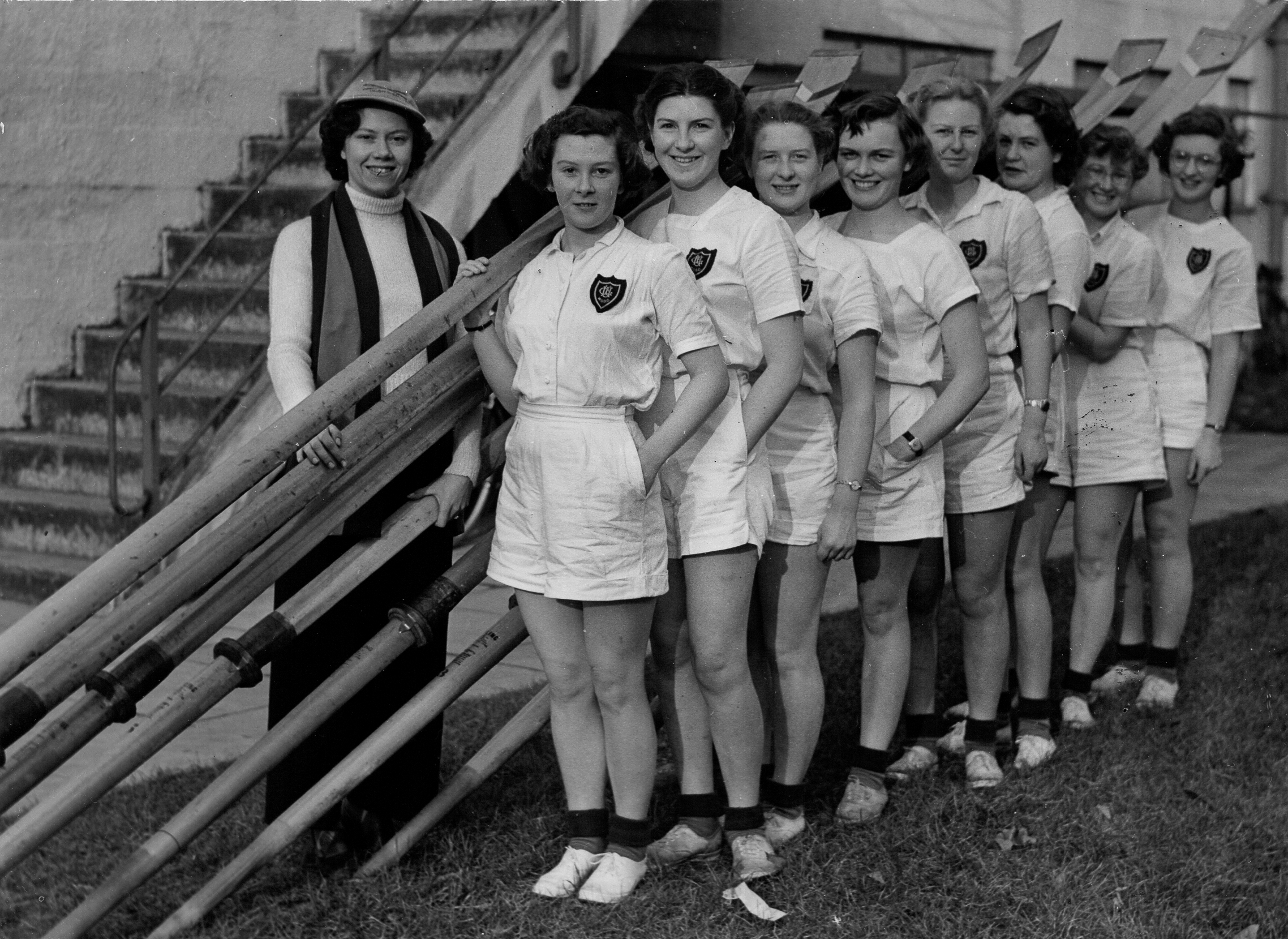 Women in white shirts and shorts with blades by boathouse