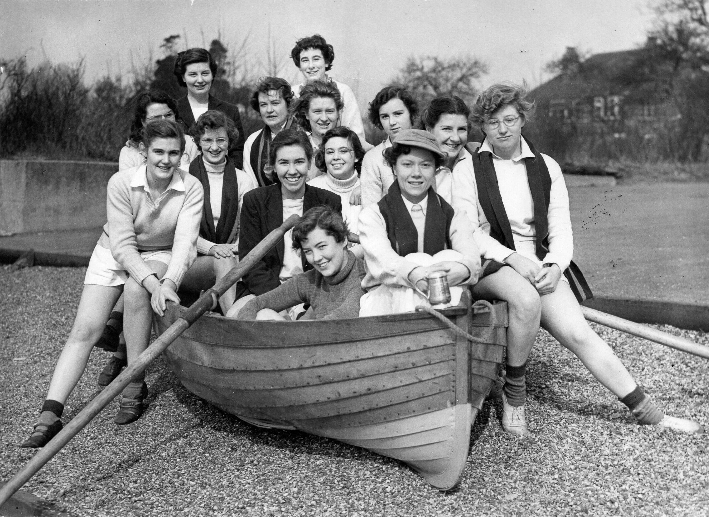 Women in rowing kit sitting in a dinghy on gravel