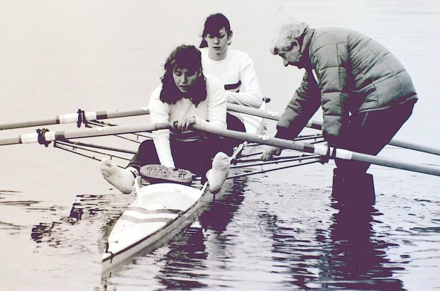 b/w photo of two women getting in double scull with male coach holding boat
