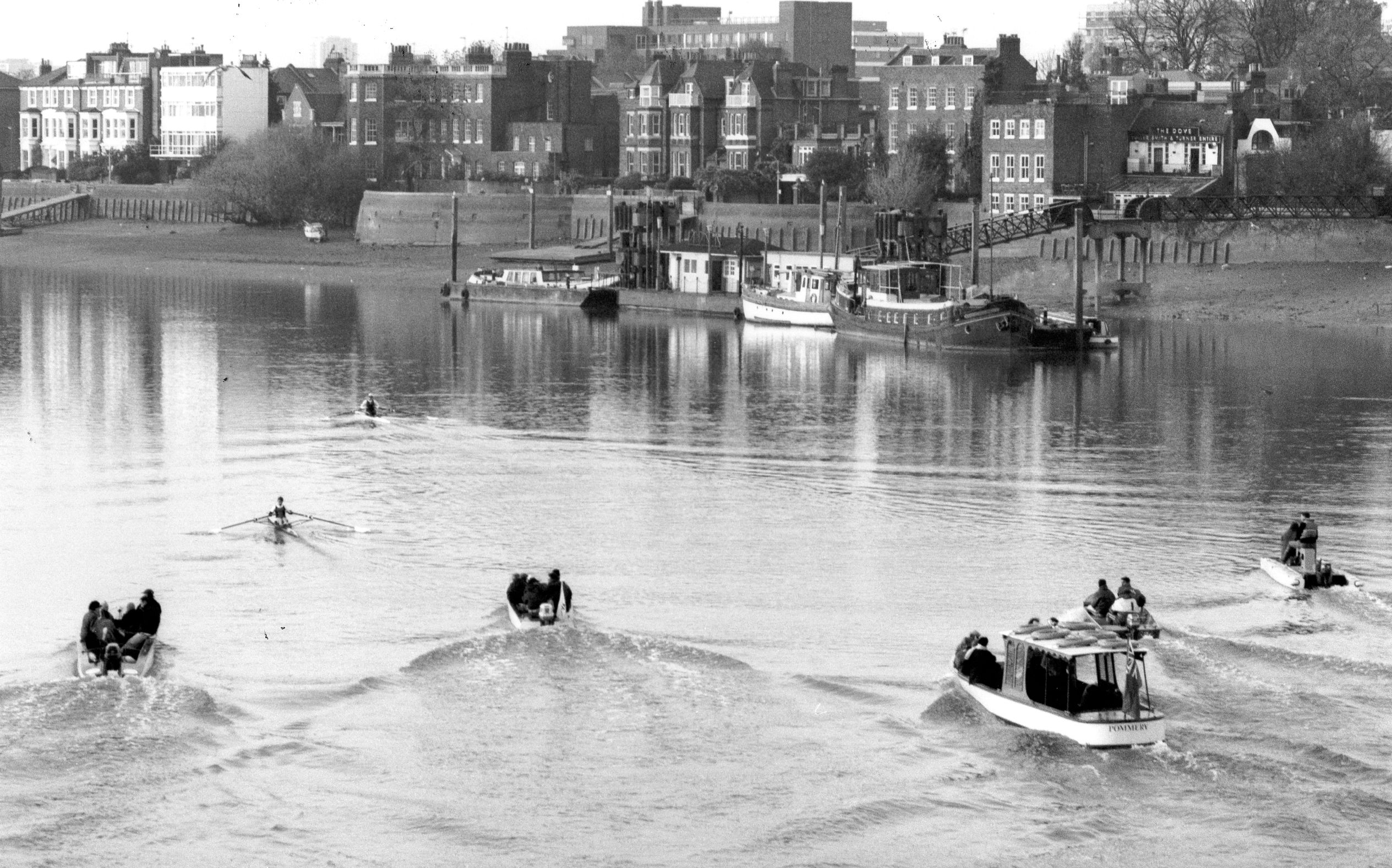b/w photo of 2 scullers passing Dove Pier pursued by 5 launches
