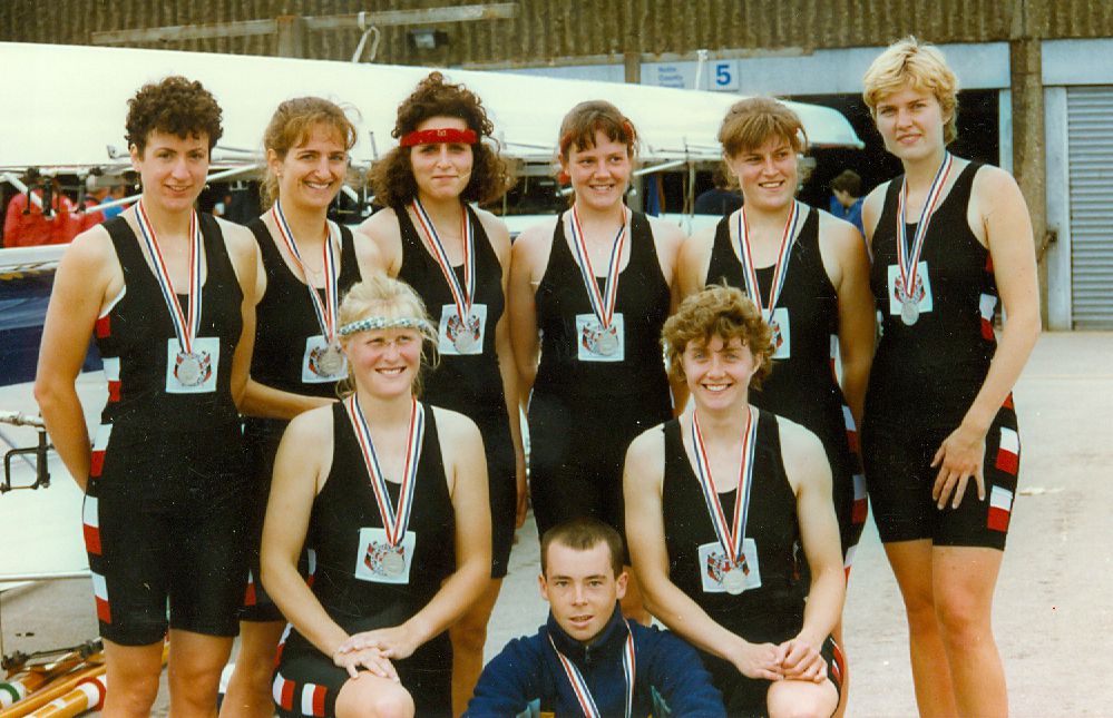Women's eight standing by boat rack wearing slver edals
