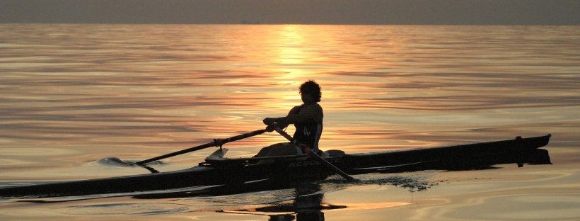 woman scullling with sunset in background