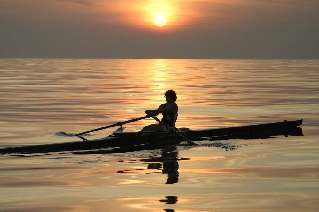 woman sculling with sunset in background