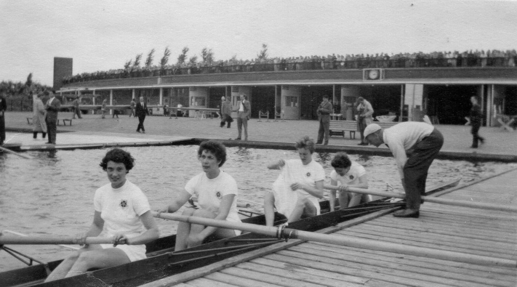 Women's four being pulled in to landing stage by by male coach